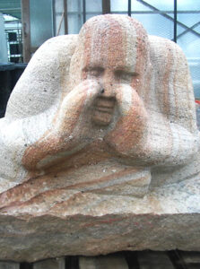 Hockender Mensch im Schneidersitz, beide Hände zum flüstern an den Mund gelegt