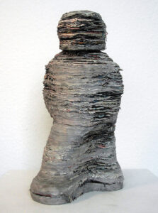 Einzelne Blätter von Illustrierten aufeinander geklebt, nach dem Trocknen in Form eines schreitenden, stilisierten Mensch geschnitzt